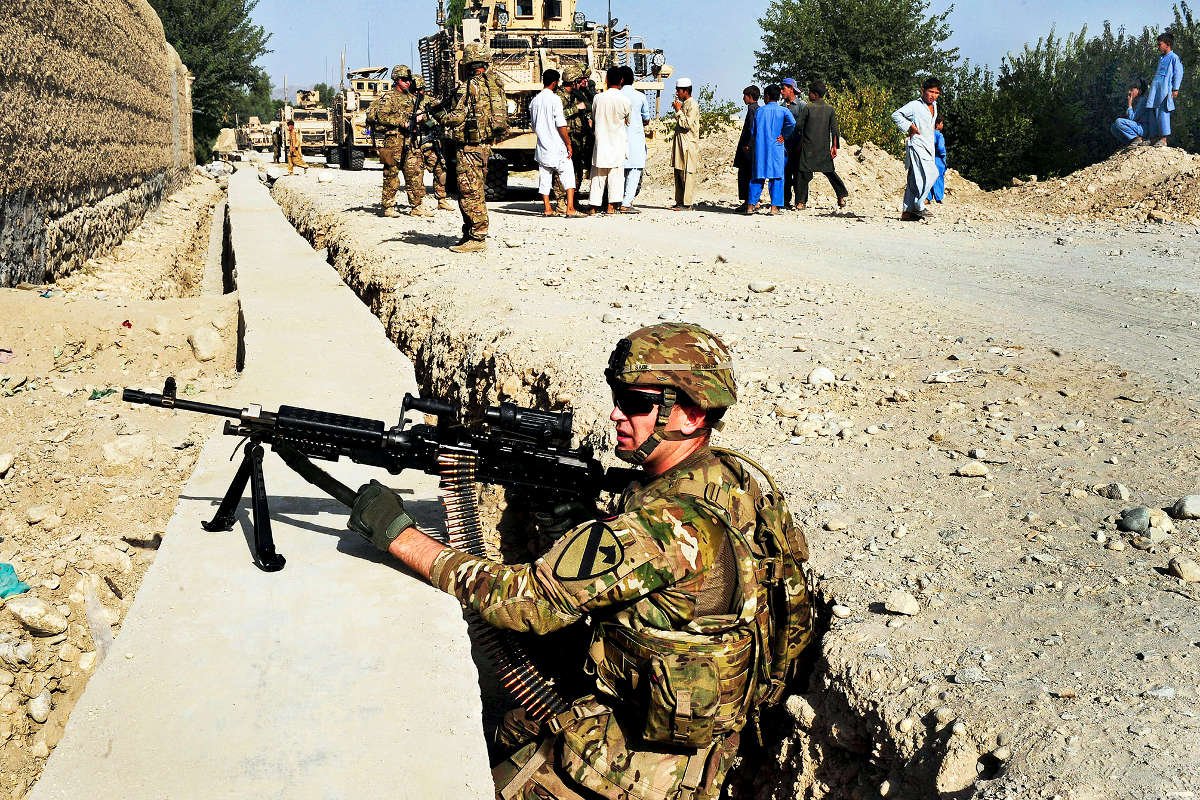 A soldier pulls security while others conduct interviews.